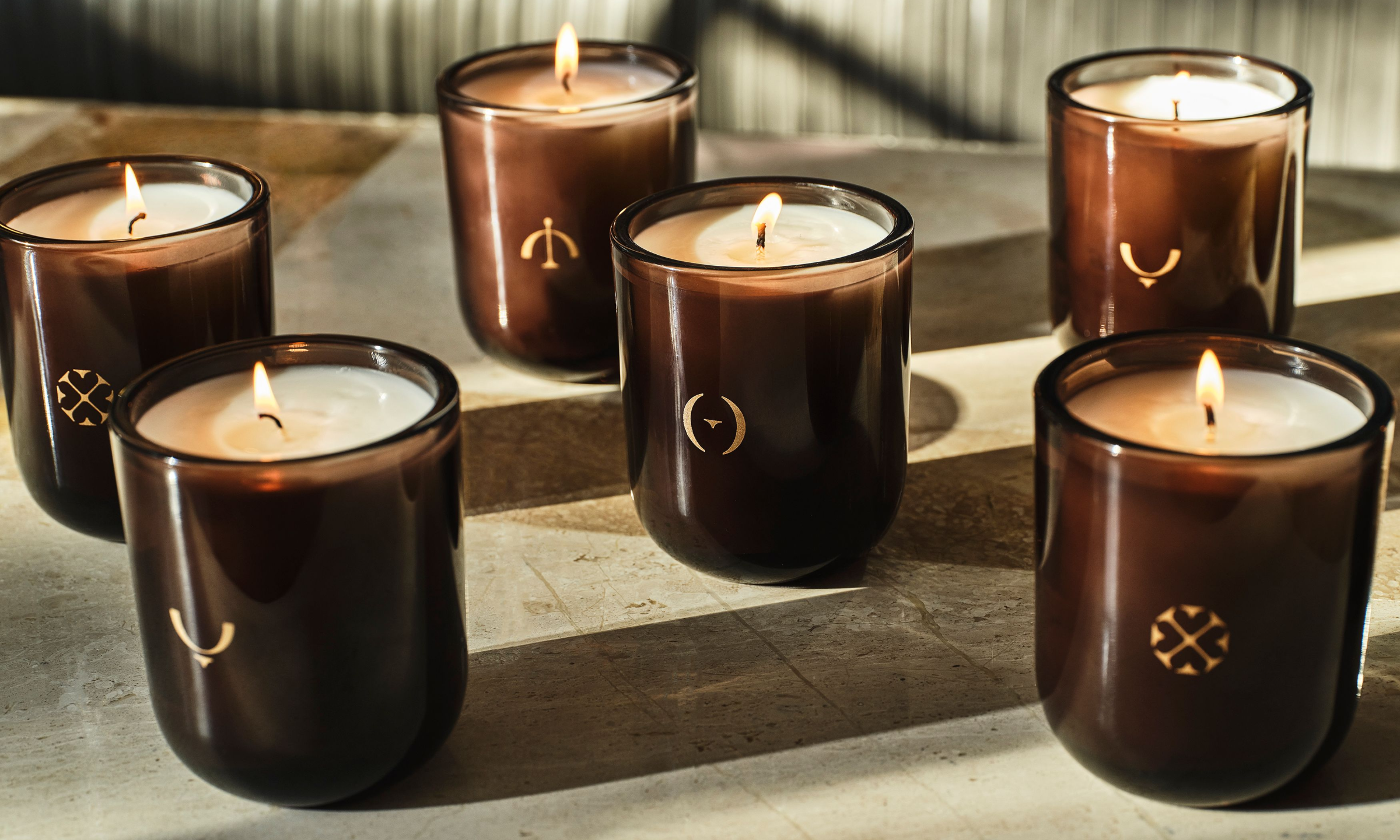 6 lit candles in brown glass tumblers with gold seasonal symbols